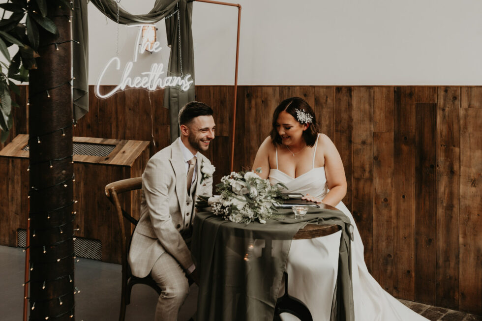 Newly married bride and groom signing the wedding register under personalised neon sign at The River Mill