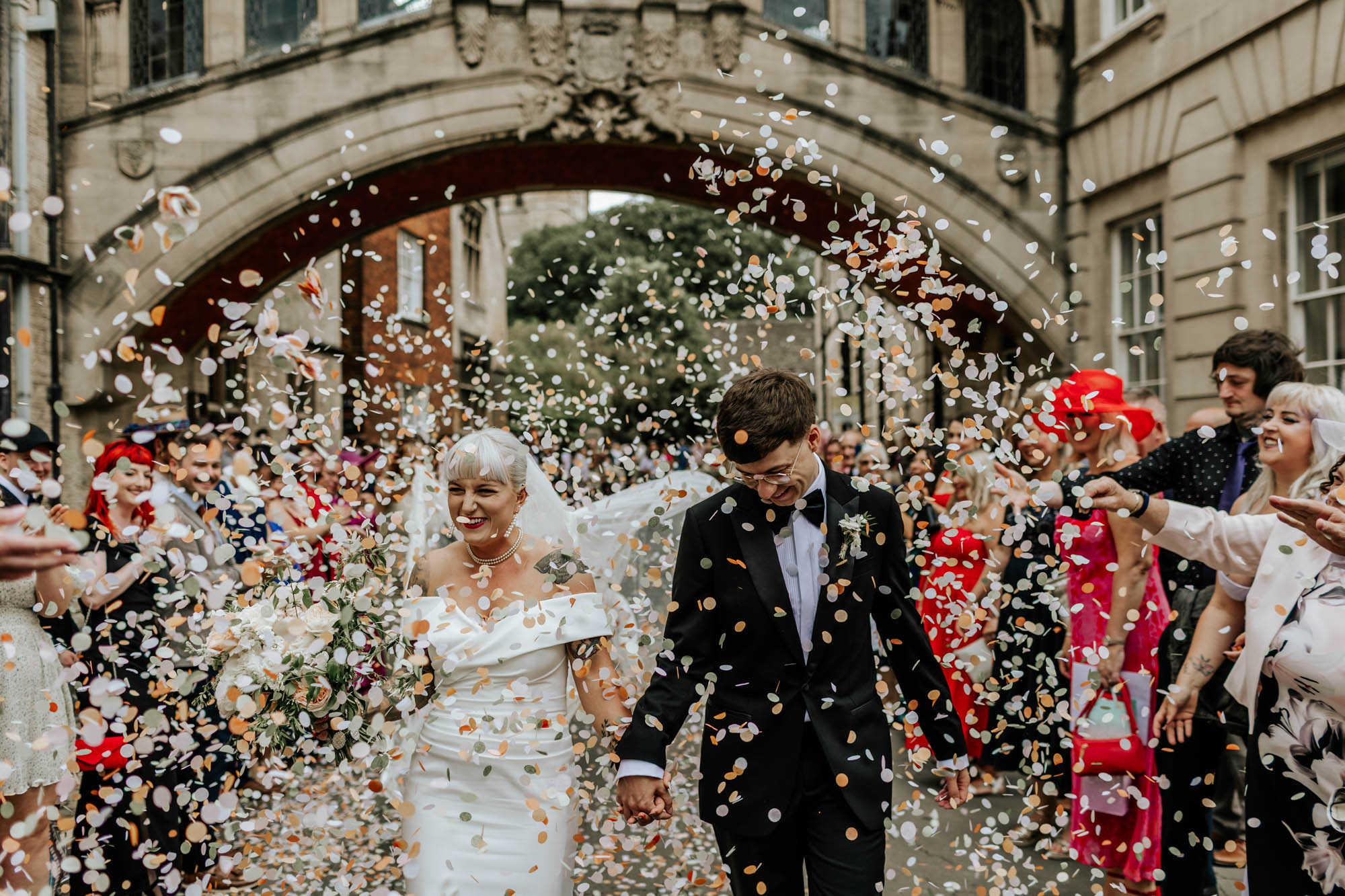 Lauren_Brumby_Photography_Bodleian_Library_Oxford Bride and groom walk through confetti outside the Bodleian Library, Oxford, underneath the Bridge of Sighs, surrounded by cheering guests.